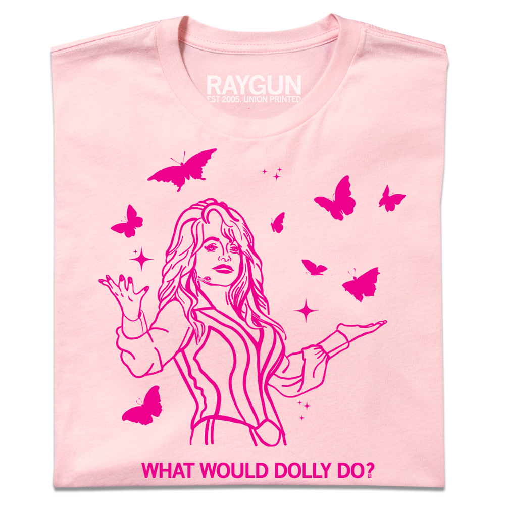 A folded pastel pink t-shirt with hot pink ink depicting Dolly Parton with open arms, surrounding by butterflies and sparkles. All caps text below says, "WHAT WOULD DOLLY DO?"