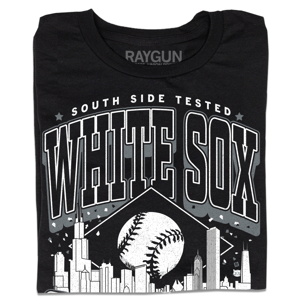 A folded black t-shirt with white ink. Text reads "South Side tested. White Sox Chicago. Pope approved." with the Chicago skyline in the center and a baseball above it.