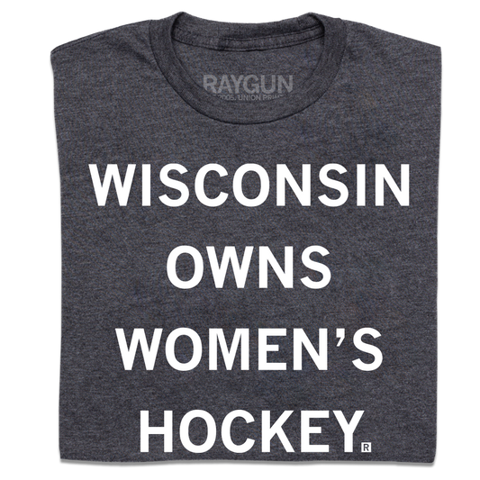A folded heather charcoal t-shirt with centered white ink text that reads "Wisconsin owns women's hockey."