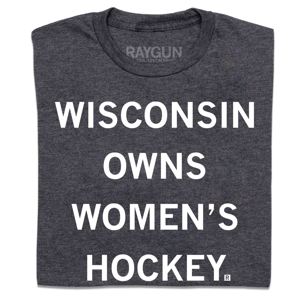 A folded heather charcoal t-shirt with centered white ink text that reads "Wisconsin owns women's hockey."