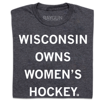 A folded heather charcoal t-shirt with centered white ink text that reads "Wisconsin owns women's hockey."