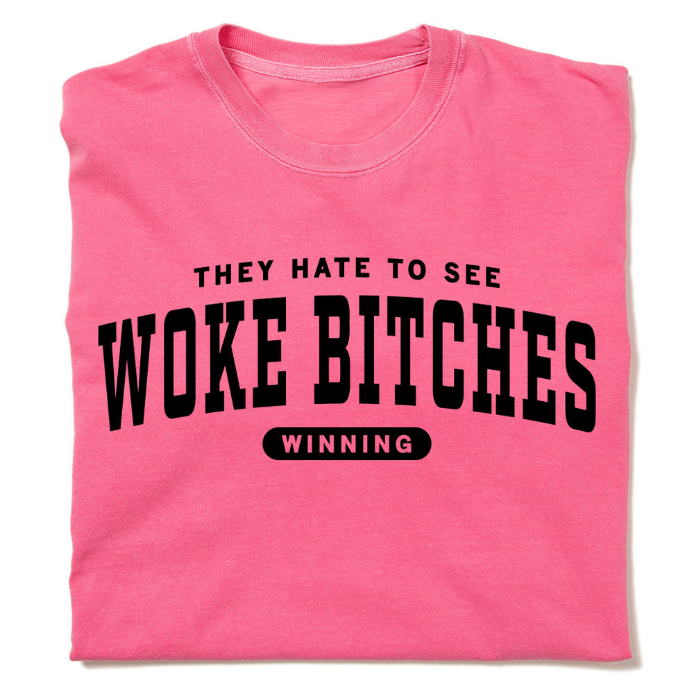 A folded crunchberry heavyweight t-shirt with black ink text that reads "They hate to see woke bitches winning"
