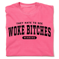 A folded crunchberry heavyweight t-shirt with black ink text that reads "They hate to see woke bitches winning"