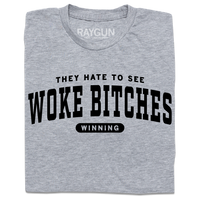 A folded heather grey t-shirt with black ink text that reads "They hate to see woke bitches winning"