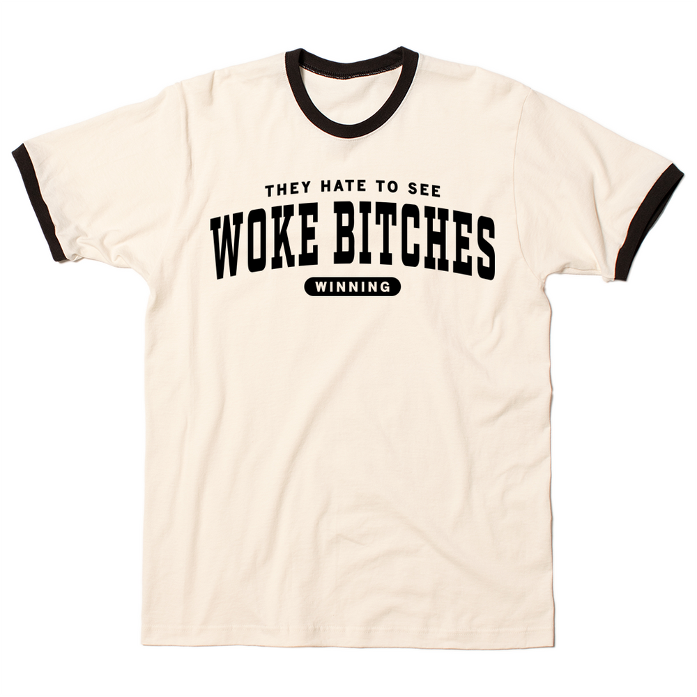Ringer t-shirt with a cream base, black collar, and black around the sleeves. Centered black ink text says, "A folded heather grey t-shirt with black ink text that reads "They hate to see woke bitches winning"