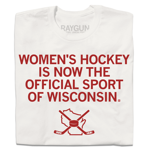 A folded off white t-shirt with centered red in text that reads "Women's Hockey is now the Official Sport of Wisconsin" over an outline of Wisconsin with crossed hockey sticked and a puck centered on top of it.