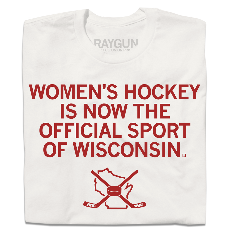 A folded off white t-shirt with centered red in text that reads "Women's Hockey is now the Official Sport of Wisconsin" over an outline of Wisconsin with crossed hockey sticked and a puck centered on top of it.
