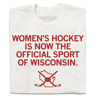 A folded off white t-shirt with centered red in text that reads "Women's Hockey is now the Official Sport of Wisconsin" over an outline of Wisconsin with crossed hockey sticked and a puck centered on top of it.