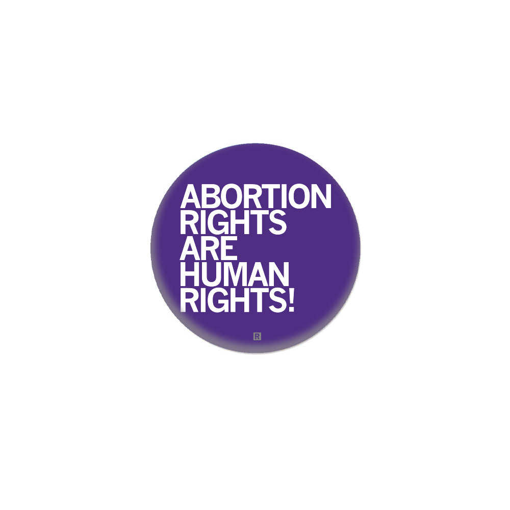 A round purple metal button with white text that reads, ABORTION RIGHTS ARE HUMAN RIGHTS!.