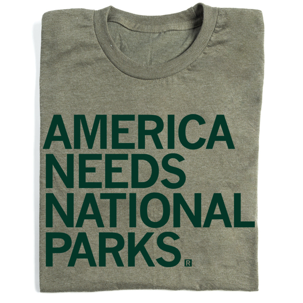 Folded heather military green t-shirt with forest green text that reads "America Needs National Parks"