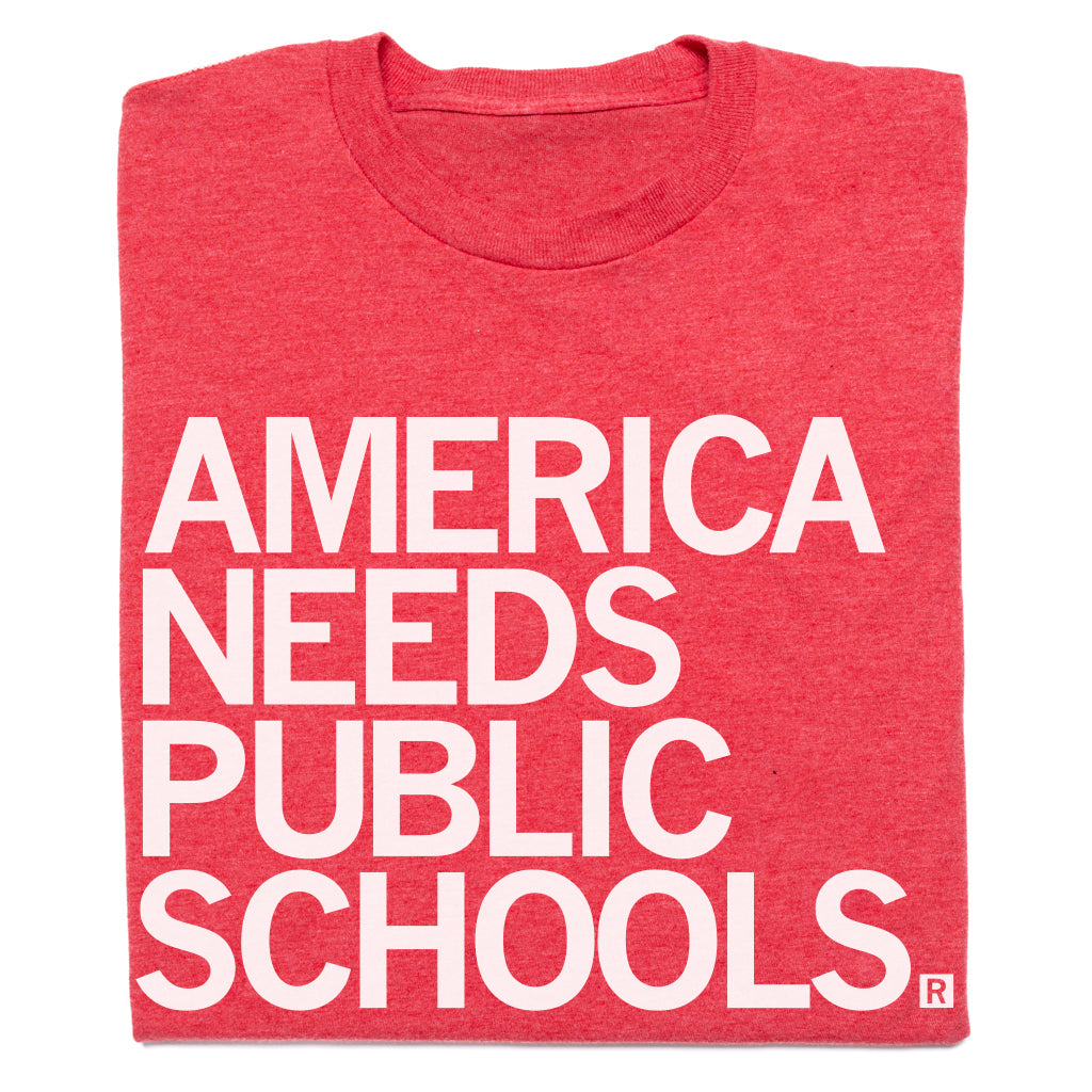 Folded red t-shirt with white text 'AMERICA NEEDS PUBLIC SCHOOLS' on a white background