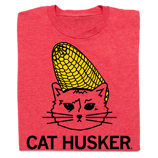 Heather red RAYGUN t-shirt featuring a graphic of Gary the Cat Husker, a cat wearing a corn cob on its head with the text CAT HUSKER printed below.