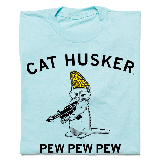 Heather purist blue t-shirt featuring a graphic of a cat wearing a corn cob hat and holding a laser gun, with the text CAT HUSKER above and PEW PEW PEW below.