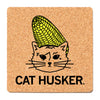 Square RAYGUN cork coaster featuring a black line drawing of a cat with a yellow ear of corn on its head, with the text CAT HUSKER below.