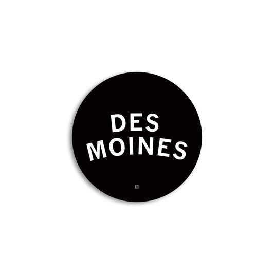 Black circular Des Moines logo with the words in white sans-serif capital letters on a vinyl sticker.