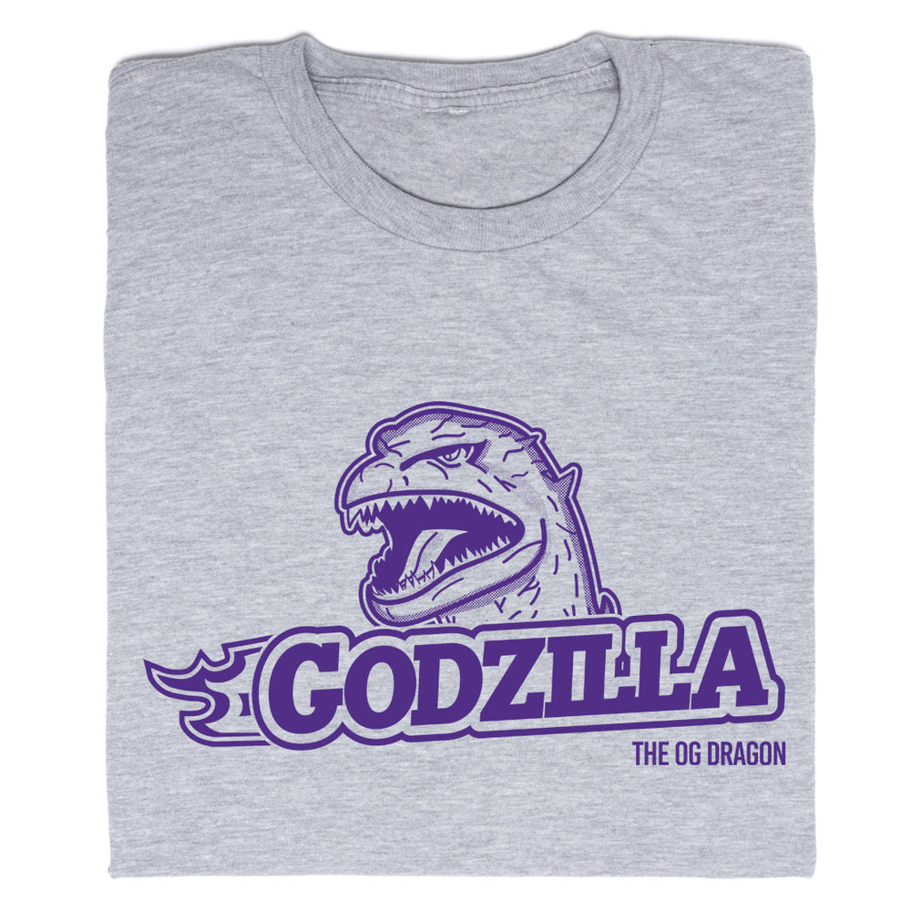 A folded heather grey t-shirt with purple ink that says, "Godzilla The OG Dragon" with Godzilla's head emerging above the text.
