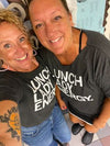 Two smiling women wearing matching charcoal t-shirts that say Lunch Lady Energy in large white letters.