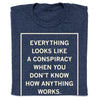 Folded navy blue shirt with cream ink that reads "Everything Looks Like A Conspiracy When You Don't Know How Anything Works."