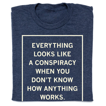 Folded navy blue shirt with cream ink that reads "Everything Looks Like A Conspiracy When You Don't Know How Anything Works."