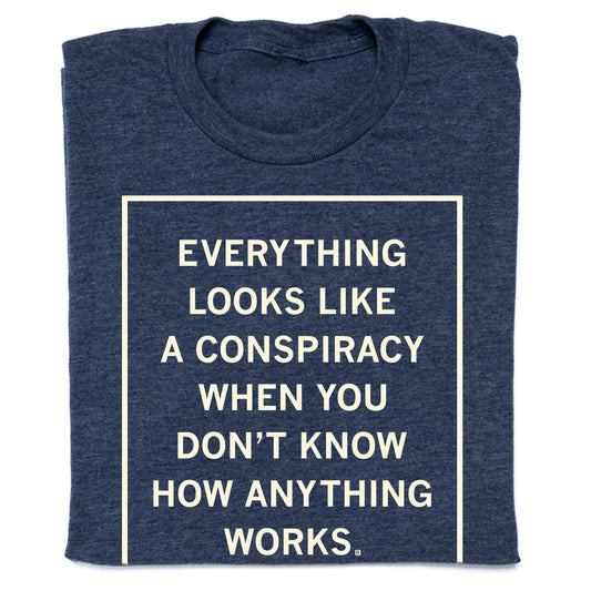Folded navy blue shirt with cream ink that reads "Everything Looks Like A Conspiracy When You Don't Know How Anything Works."