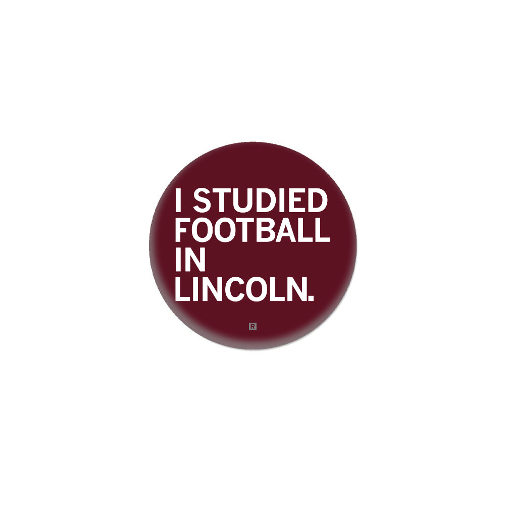 Maroon circular RAYGUN button with the white text I STUDIED FOOTBALL IN LINCOLN.