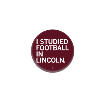 Maroon circular RAYGUN button with the white text I STUDIED FOOTBALL IN LINCOLN.