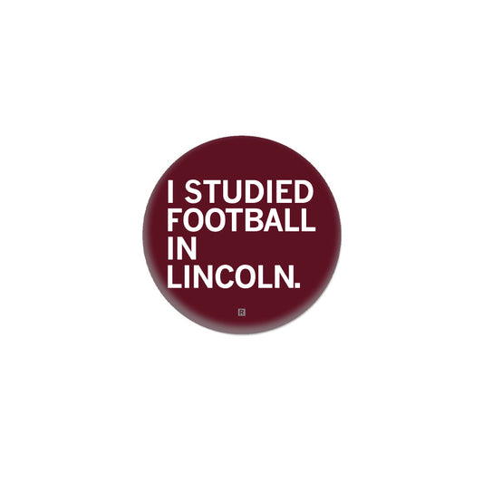 Maroon circular RAYGUN button with the white text I STUDIED FOOTBALL IN LINCOLN.