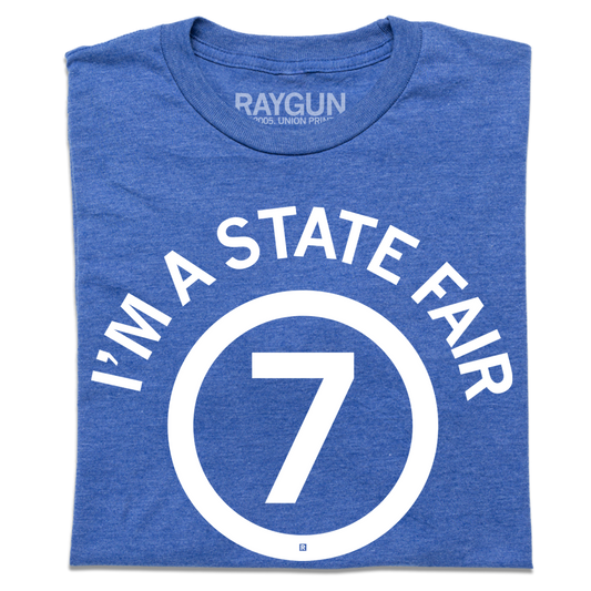 Heather royal blue t-shirt featuring the white text IM A STATE FAIR in a circle around the number 7.