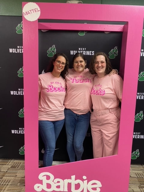Three women pose inside a pink Barbie-themed frame, wearing union made t-shirts with text that reads My job is books or My job is teach.