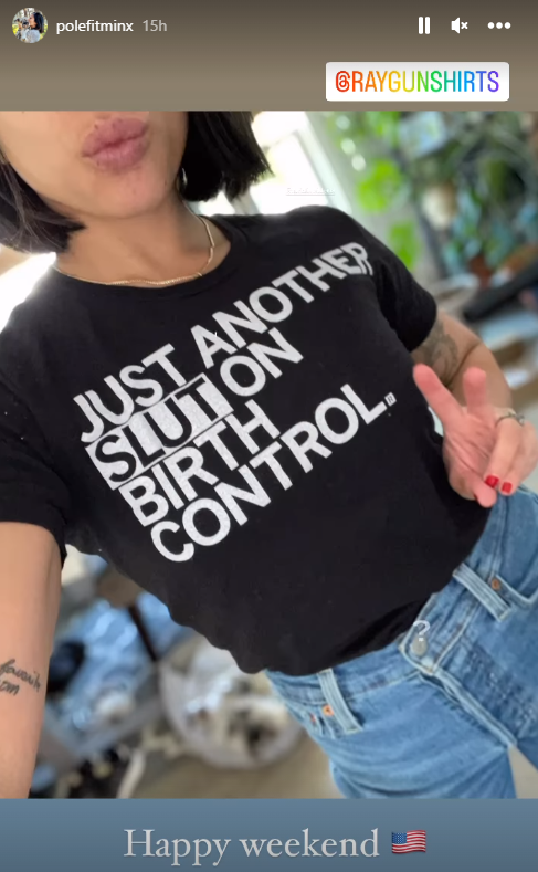 A person wearing a union-made black t-shirt that says JUST ANOTHER SLUT ON BIRTH CONTROL with a hand making a peace sign.