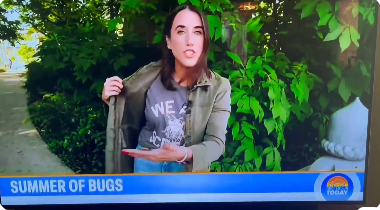 A news reporter outdoors holds open her jacket to reveal a RAYGUN t-shirt, with a chyron at the bottom reading SUMMER OF BUGS.