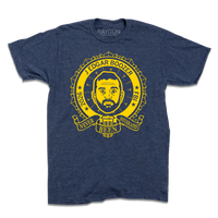 Heather navy t-shirt with bright yellow ink illustrating a ribbon around an image of Kash Patel. Text reads "2026 J Edgar Boozer FBI. Never been intoxicated" with small martini glasses and beer bottles circling his head.