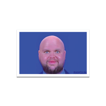 A die-cut vinyl sticker portrait of a bald, bearded man with wide blue eyes against a blue background, with the word RAYGUN in the bottom right corner.