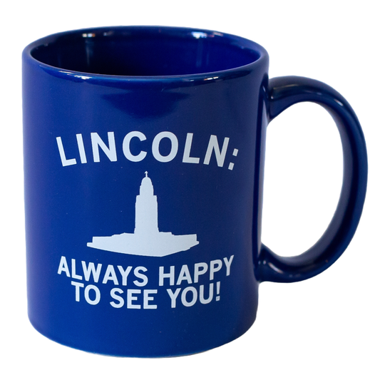Blue, dishwasher-safe ceramic mug featuring white text that reads LINCOLN: ALWAYS HAPPY TO SEE YOU! above a white silhouette of the Nebraska State Capitol building.