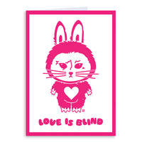 A white card with a hot pink border and image of RAYGUN's cat mascot dressed like a labubu above the text "Love is blind"