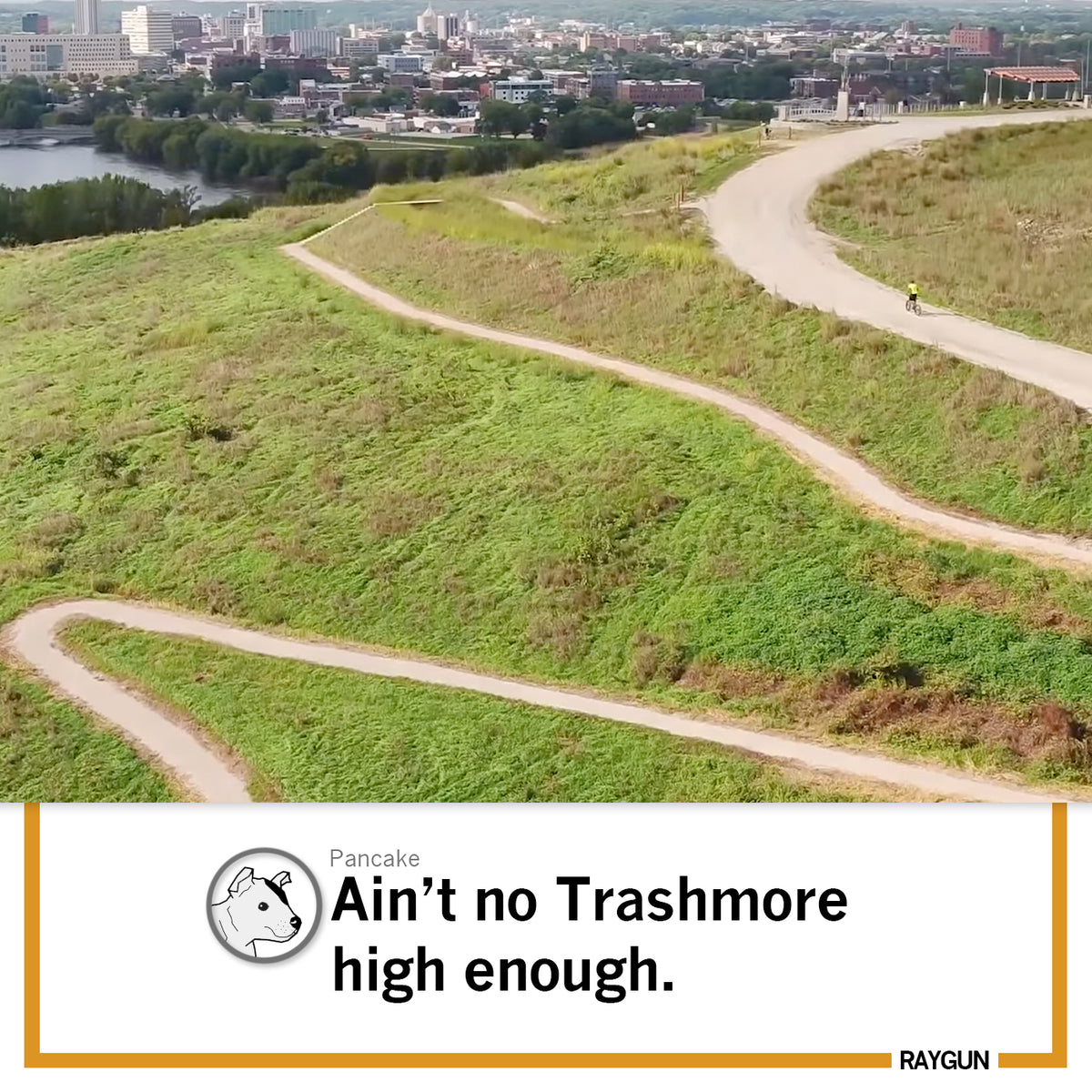 A cyclist in a white t-shirt rides on a winding trail atop a grassy hill overlooking Cedar Rapids, with text overlay reading Pancake Aint no Trashmore high enough.