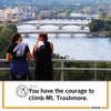 Two people wearing Cedar Rapids T-shirts lean against a railing overlooking a river and bridges, with the text You have the courage to climb Mt. Trashmore.
