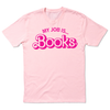 A short sleeve light pink t-shirt with hot pink ink text that says, "My Job Is...Books" with "Books" being in Barbie font.