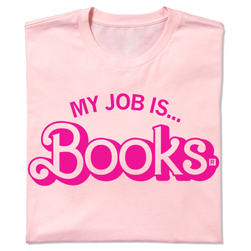 A folded light pink t-shirt with hot pink ink text that says, "My Job Is...Books" with "Books" being in Barbie font.