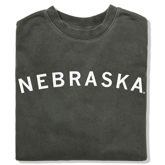 Folded charcoal gray RAYGUN crewneck sweatshirt with the word NEBRASKA printed in white arching across the chest.