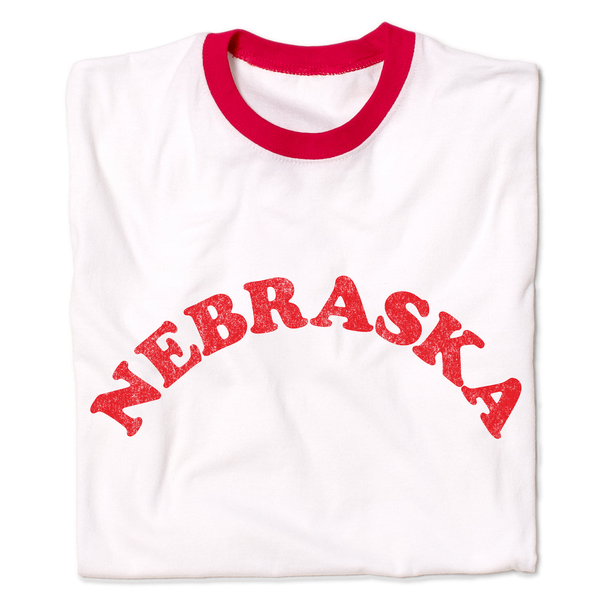 White ringer T-shirt with a red neckline and the word NEBRASKA printed in a red, arched, distressed font across the chest, representing the Cornhusker State.