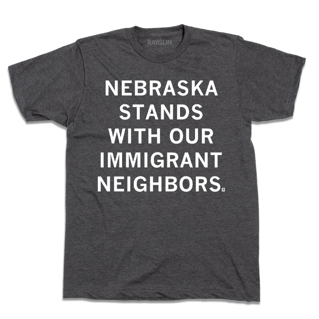 Dark gray union-made t-shirt featuring the white text NEBRASKA STANDS WITH OUR IMMIGRANT NEIGHBORS in support of Nebraska immigrant communities.