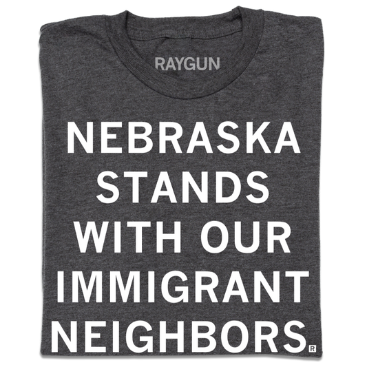 Dark gray union-made t-shirt featuring the text NEBRASKA STANDS WITH OUR IMMIGRANT NEIGHBORS in white block letters.
