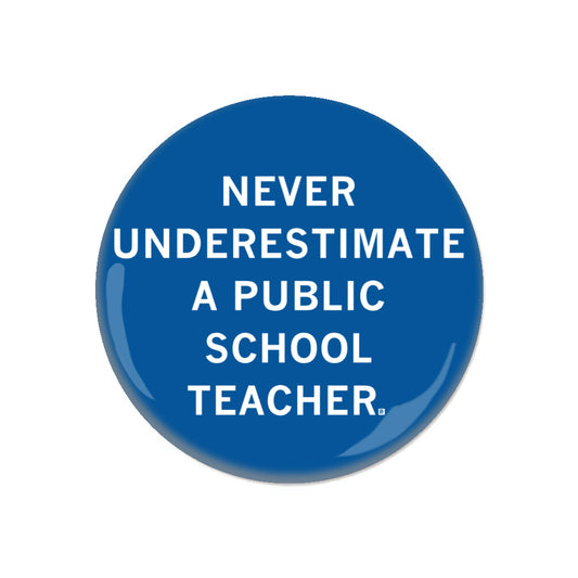 Blue circular RAYGUN metal button with white text that reads, NEVER UNDERESTIMATE A PUBLIC SCHOOL TEACHER.