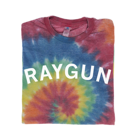 Folded rainbow tie-dyed t-shirt with RAYGUN printed in white letters.