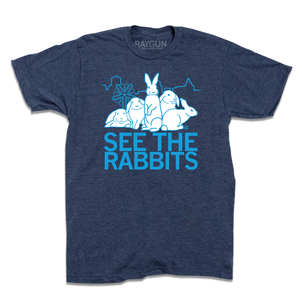 Heather denim t-shirt featuring a graphic of four white rabbits in front of a Cedar Rapids skyline outline with the text SEE THE RABBITS in light blue.