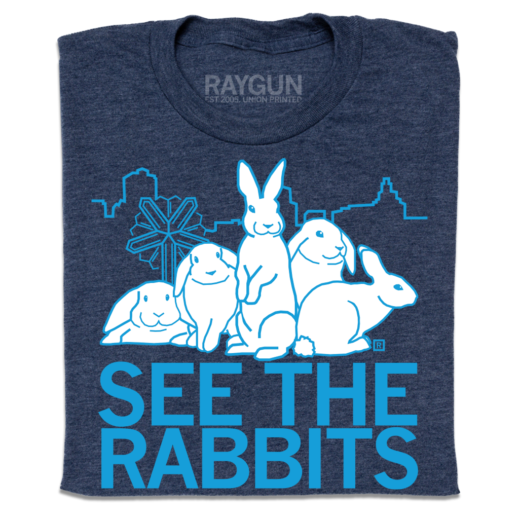 Heather denim t-shirt featuring a white graphic of four rabbits in front of a city skyline, with the text SEE THE RABBITS below in light blue.
