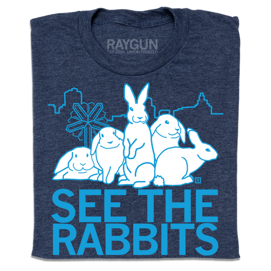 Heather denim t-shirt featuring a white graphic of four rabbits in front of a city skyline, with the text SEE THE RABBITS below in light blue.