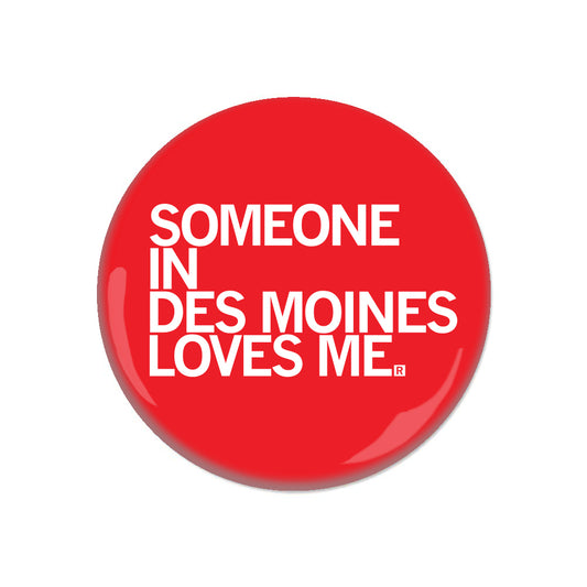 A round, red metal button featuring the white text, SOMEONE IN DES MOINES LOVES ME.