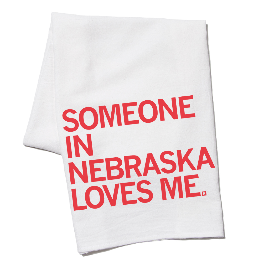 A white flour sack towel printed with the red text SOMEONE IN NEBRASKA LOVES ME.
